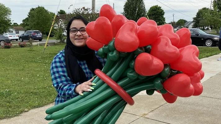 A volunteer smiling and holding a giant bouquet of red heart-shaped balloons that volunteers handed out for Operation Eid