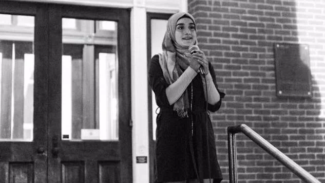 Sarah Alzabet speaking into a microphone outside a brick building at the We All Belong peace rally in downtown Murfreesboro